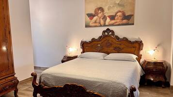 A bedroom with a wooden four-poster bed, two bedside tables with lamps, a wooden wardrobe, and a painting on the wall.