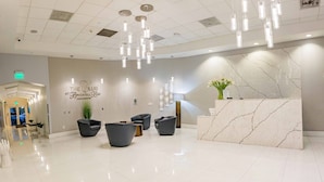 A modern reception area with a marble reception desk, black leather chairs, and a sign reading "The Club at Brickell Bay Condominium".