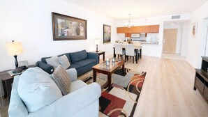 A modern living room with a sofa, a dining table, and a kitchen in the background.