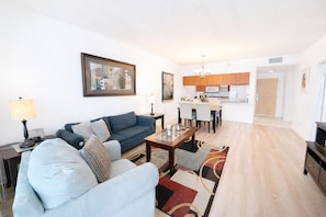 A modern living room with a sofa, a dining table, and a kitchen in the background. - 1BD beautiful view, free parking (Miami)