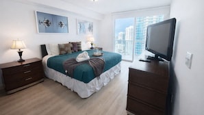 A modern hotel room with a bed, bedside tables, a TV, and a large window with a city view.