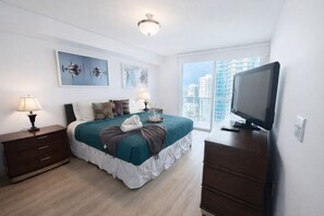 A modern hotel room with a bed, bedside tables, a TV, and a large window with a city view.