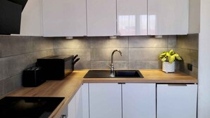 Una cocina moderna con armarios blancos, un tostador negro, un fregadero y una planta en maceta.