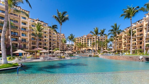 Ein Resort mit einem großen Swimmingpool, umgeben von Palmen und mehrstöckigen Gebäuden mit Balkonen.