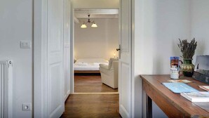 En hall som leder till ett sovrum med en säng, en stol och ett skrivbord med en vas och böcker.