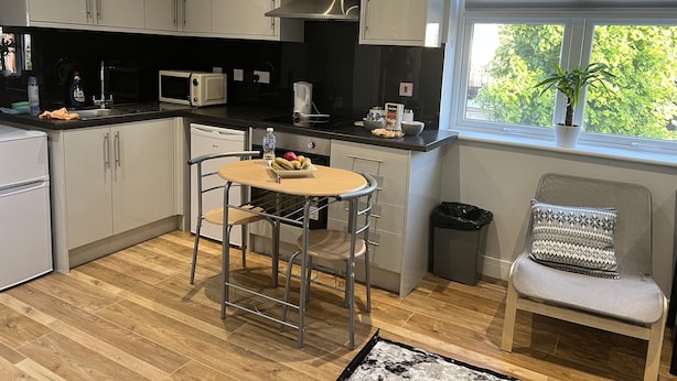 A compact kitchen with white cabinets, a microwave, a sink, and a window with blinds. - The Grand Bleu - Next to Tube station (London)