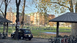 A parking area with a car and bicycles, a no parking sign, and a park in the background. - The Grand Bleu - Next to Tube station (London)