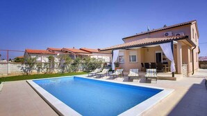 A swimming pool with lounge chairs and a covered patio area. - Villa with pool, BBQ and games room (Valbandon)