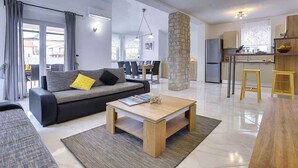 A modern living room with a sofa, coffee table, and a dining area with a kitchen in the background. - Villa with pool, BBQ and games room (Valbandon)
