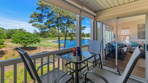 A balcony with a table and chairs, overlooking a golf course and a lake. - 3BR/2BA Pet-Friendly Condo with Pool on True Blue Golf Course (Pawleys Island)