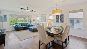 A spacious living room with a large sofa, a dining table set for six, and a ceiling fan. - 3BR/2BA Pet-Friendly Condo with Pool on True Blue Golf Course (Pawleys Island)