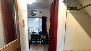 A narrow hallway with a wooden door on the left, a patterned rug on the floor, and a kitchen area with a countertop on the right.