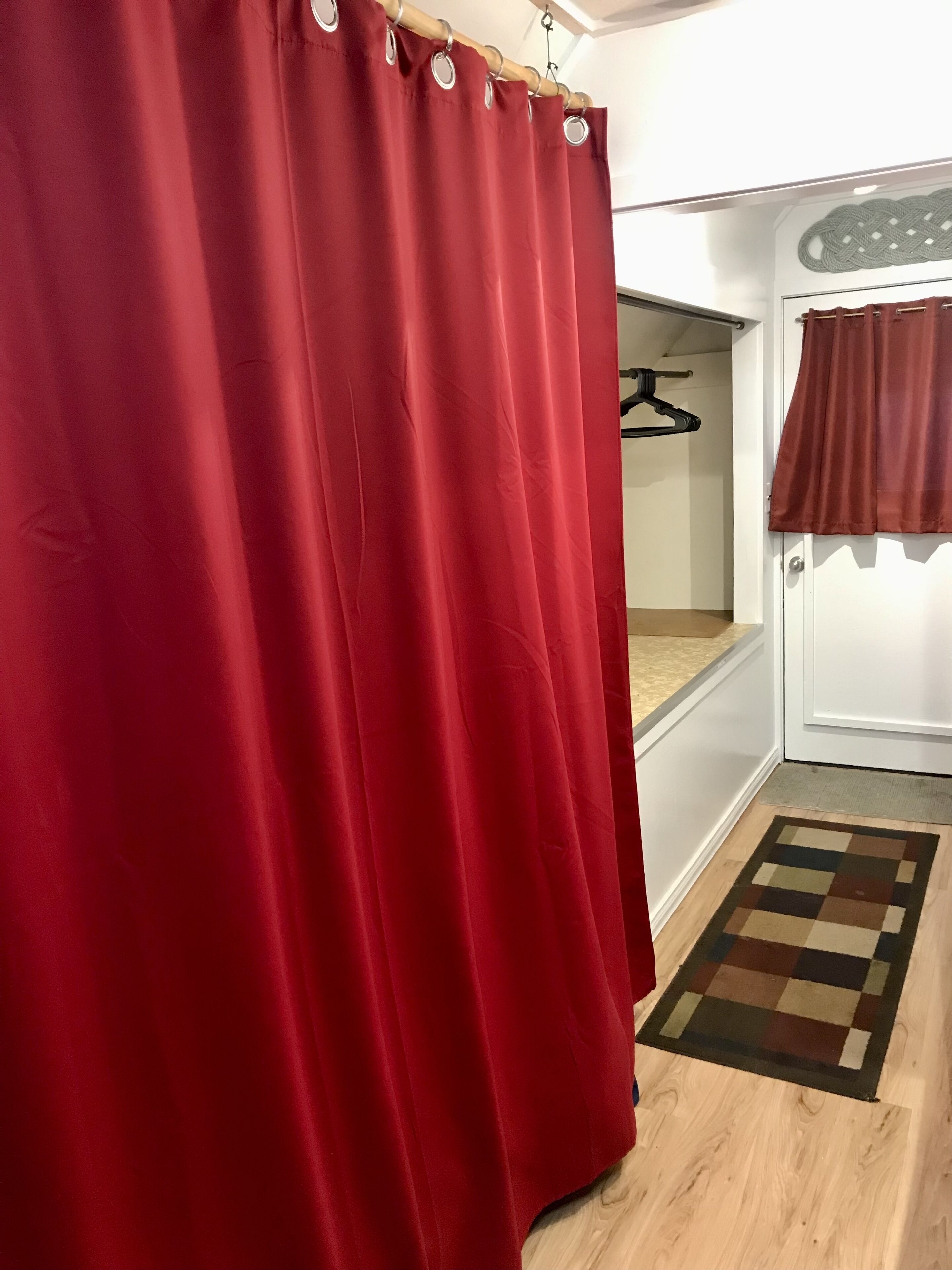 Una habitación con cortina roja, piso de madera y alfombra a cuadros.