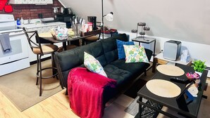 A compact living space with a kitchenette, a sofa with cushions, a coffee table, and a small side table.