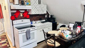 A compact kitchen with a stove, microwave, and a small dining area with a chair and table.
