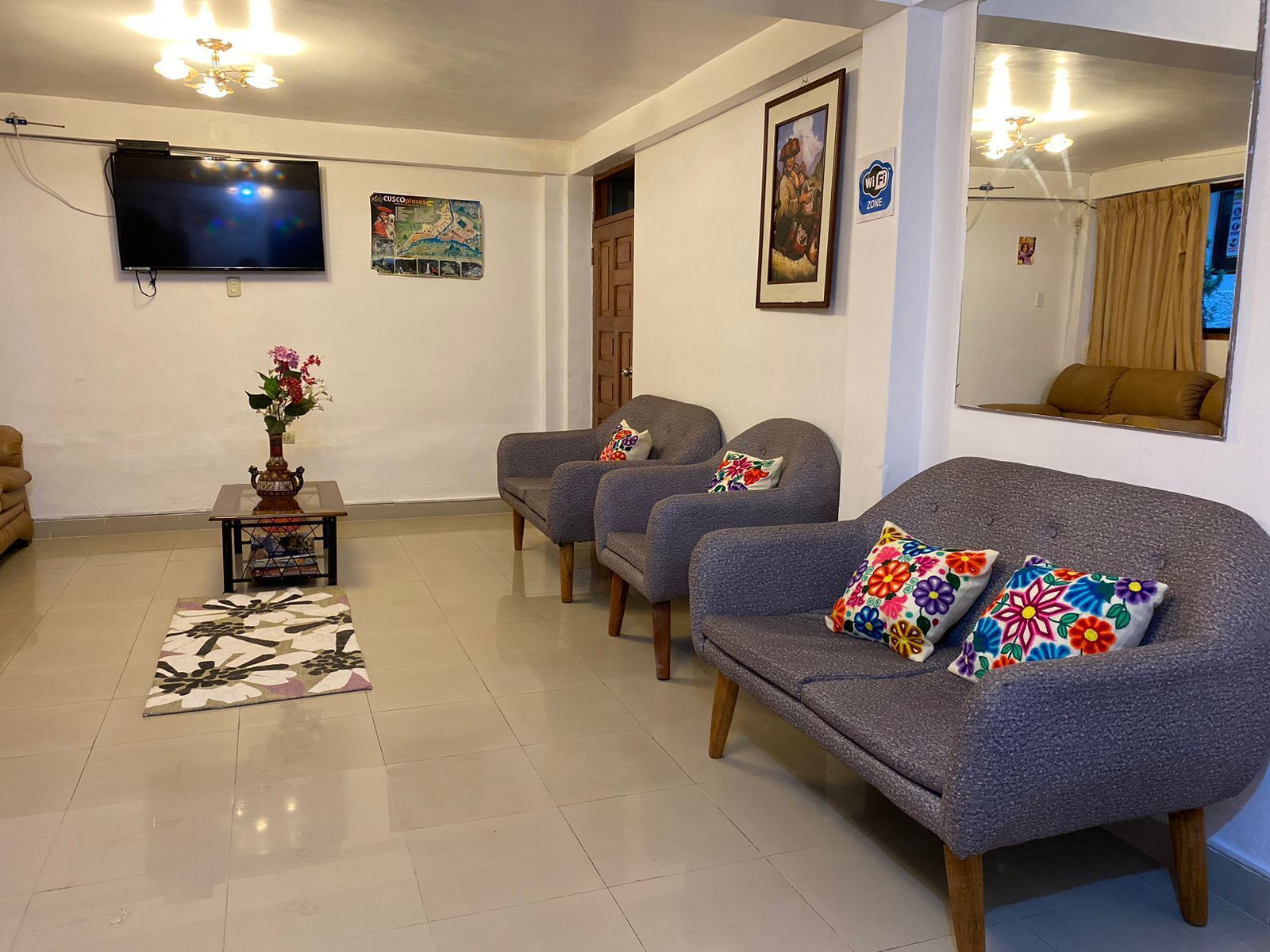 A living room with a flat-screen TV, a vase with flowers, and a sofa with colorful pillows.