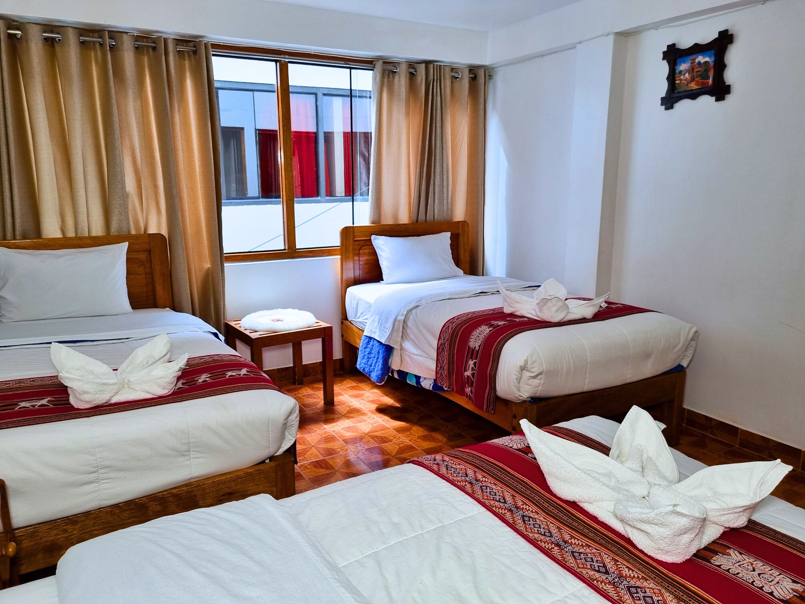 A hotel room with two beds, a small table, and a window with curtains.