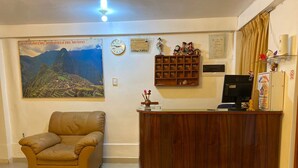 A reception area with a wooden desk, a leather sofa, a clock, a framed map, and a shelf with figurines. - Inka House Inn (Machu Picchu)