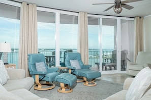 A spacious balcony with two blue reclining chairs and a beige sofa, offering a view of the cityscape.