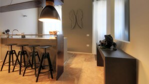 A modern kitchen with bar stools, a pendant light, and decorative wall art. - Luxury City Center Loft (Cagliari)