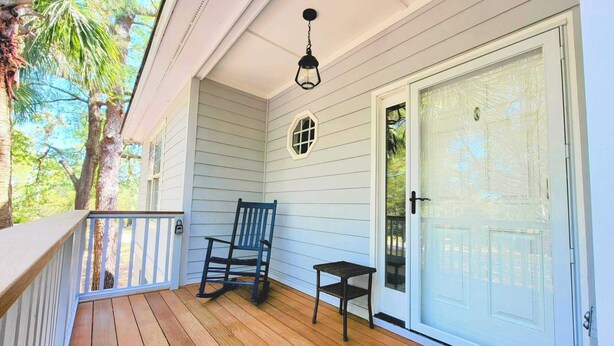 A wooden porch with a chair and table, a white door, and a hanging light fixture.