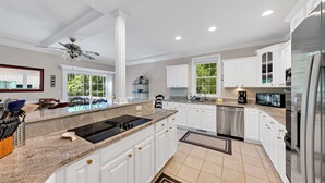 A modern kitchen with white cabinets, a granite countertop, stainless steel appliances, and a large window.