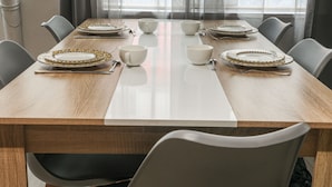 A dining table set with plates, bowls, and cutlery, surrounded by chairs.