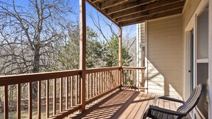 A wooden deck with a railing, a chair, and a building in the background.