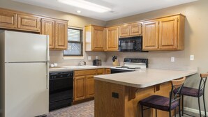 A kitchen with wooden cabinets, a refrigerator, a microwave, and a sink.