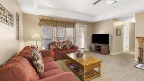 A living room with a sofa set, a coffee table, a television, and a ceiling fan.