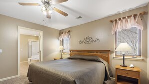 A bedroom with a bed, nightstands, a ceiling fan, a window with curtains, and a wall decoration. - Cozy Golf Condo at StoneBridge Village, minutes from Silver Dollar City! (Reeds Spring)