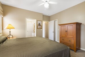 Quarto com uma cama, mesa de cabeceira com abajur, guarda-roupa e ventoinha no teto.