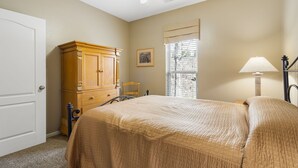 Ein Schlafzimmer mit einem Bett, einem Holzschrank, einem Stuhl, einem Fenster mit Jalousien und einem Deckenventilator.