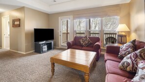 A living room with a flat-screen TV, a wooden coffee table, a red sofa, and a lamp.
