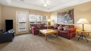 A living room with two red sofas, a wooden coffee table, a TV stand, two lamps, and a ceiling fan.