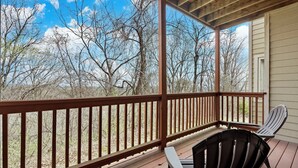 Eine überdachte Veranda mit Holzgeländer, zwei Adirondack-Stühlen und Blick auf kahle Bäume.