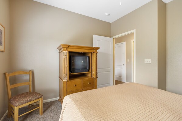 A bedroom with a bed, a wooden TV stand with a television, a chair, and a door.