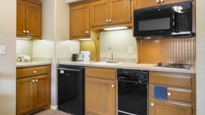 A compact kitchen with wooden cabinets, a microwave, and built-in dishwasher. - Charming Suite with Kitchenette at StoneBridge Village (Reeds Spring)