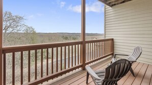 Eine überdachte Veranda mit zwei Adirondack-Stühlen, einem Holzgeländer und Blick auf eine ländliche Landschaft.
