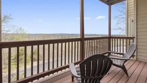 A wooden deck with two Adirondack chairs and a table, overlooking a scenic landscape. - Relaxing Condo with Fireplace, Jetted Tub, and Private Balcony (Reeds Spring)