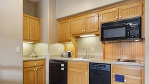 A compact kitchen with wooden cabinets, a black microwave, and a dishwasher. - Quaint Condo Suite in a Peaceful Community near Silver Dollar City (Reeds Spring)