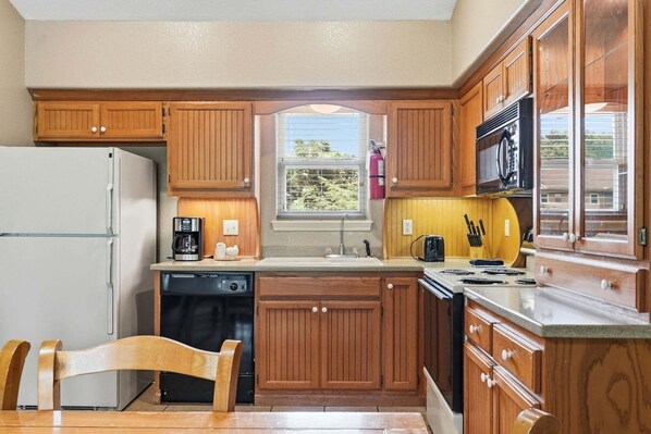 A kitchen with wooden cabinets, a refrigerator, a dishwasher, a microwave, and a window with a view of trees.