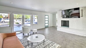 Ein geräumiges Wohnzimmer mit Kamin, einem großen an der Wand befestigten Fernseher und einer Sitzecke mit einer Couch und Sesseln.