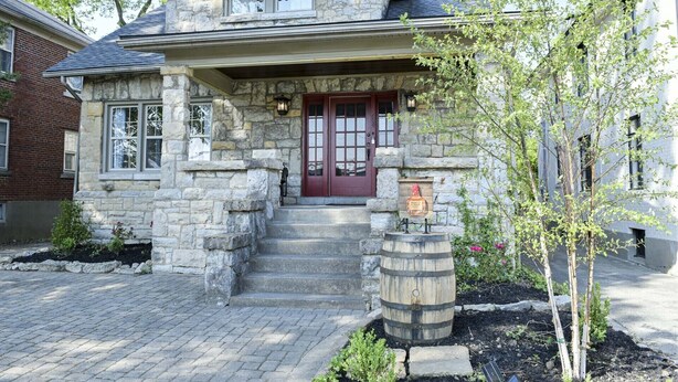 A stone house with a red door, a wooden barrel, and a small garden.