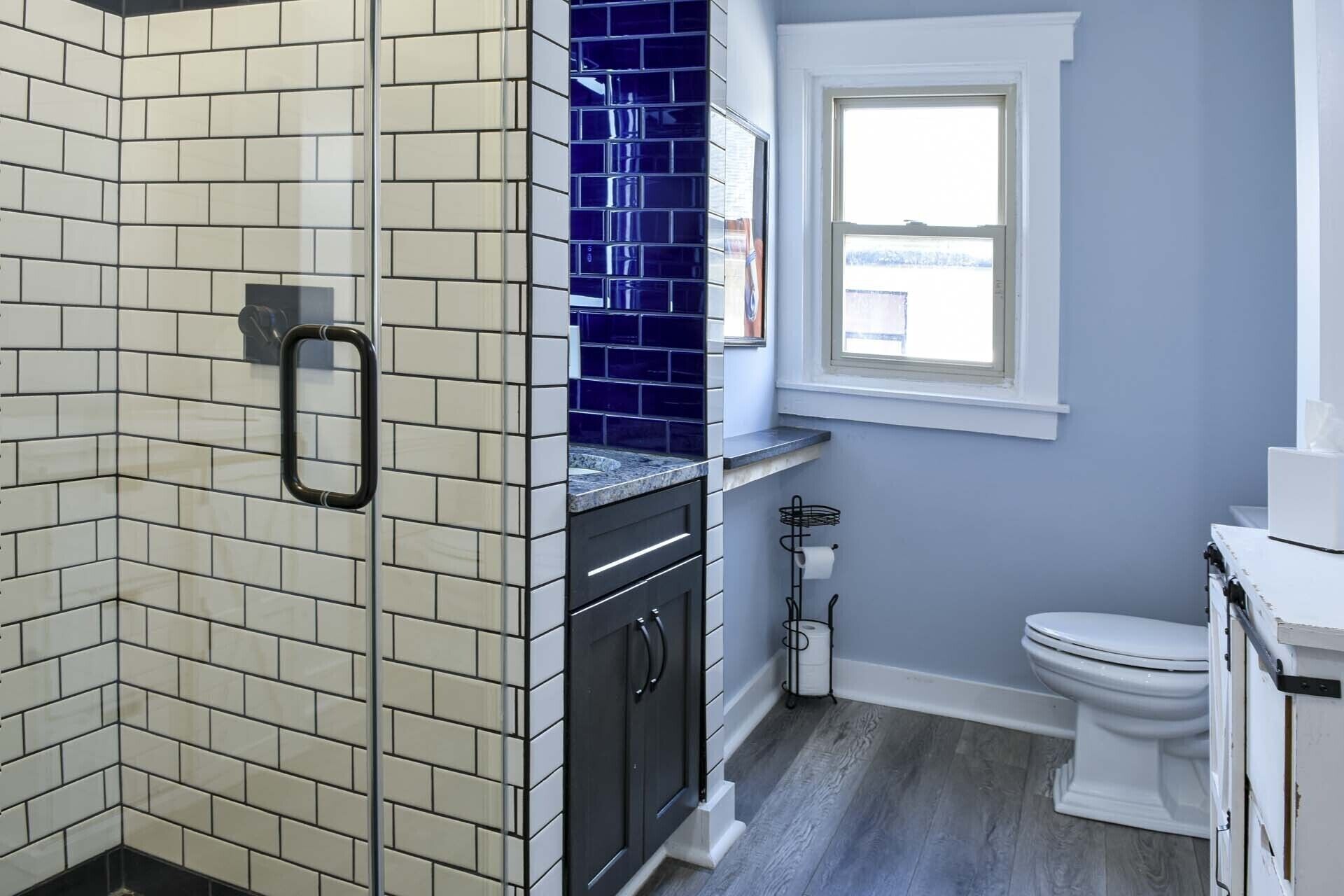 Un baño con baldosas blancas y azules, un inodoro blanco y una ventana.