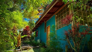 A traditional house with a wooden roof, surrounded by lush greenery and a small garden. - Las Palomas Villas (Cahuita)