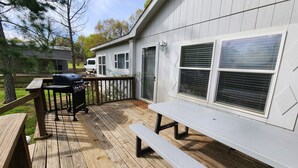 A wooden deck with a barbecue grill, a picnic table, and a covered area with a sliding door. - Cattlemens Quarters beautiful ranch setting with fenced yards and a great deck! (Tyler)