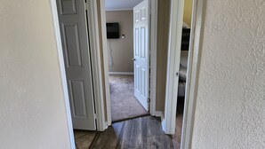 A hallway with a carpeted floor, white walls, and a door leading to another room. - Cattlemens Quarters beautiful ranch setting with fenced yards and a great deck! (Tyler)
