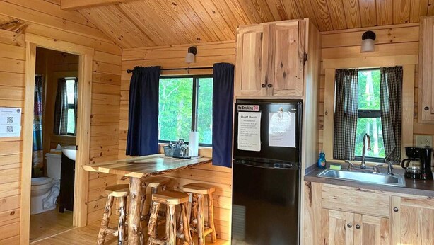 A wooden cabin with a kitchen area, including a refrigerator, sink, and bar stools. - 114) Pelican Log Cabin. Close to Hocking Hills State Park and more! (Logan)