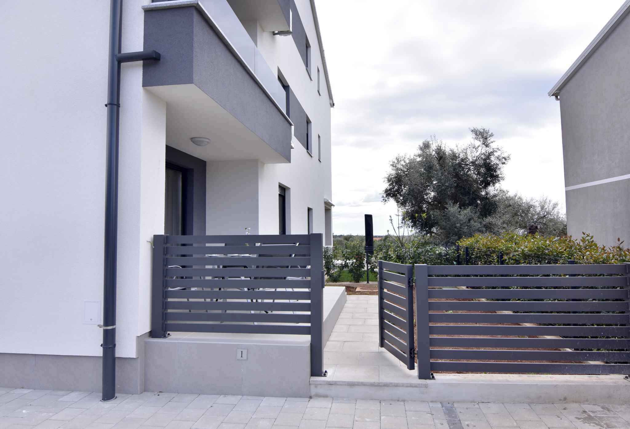 A modern residential building with a gated entrance, a flat roof, and a paved driveway.